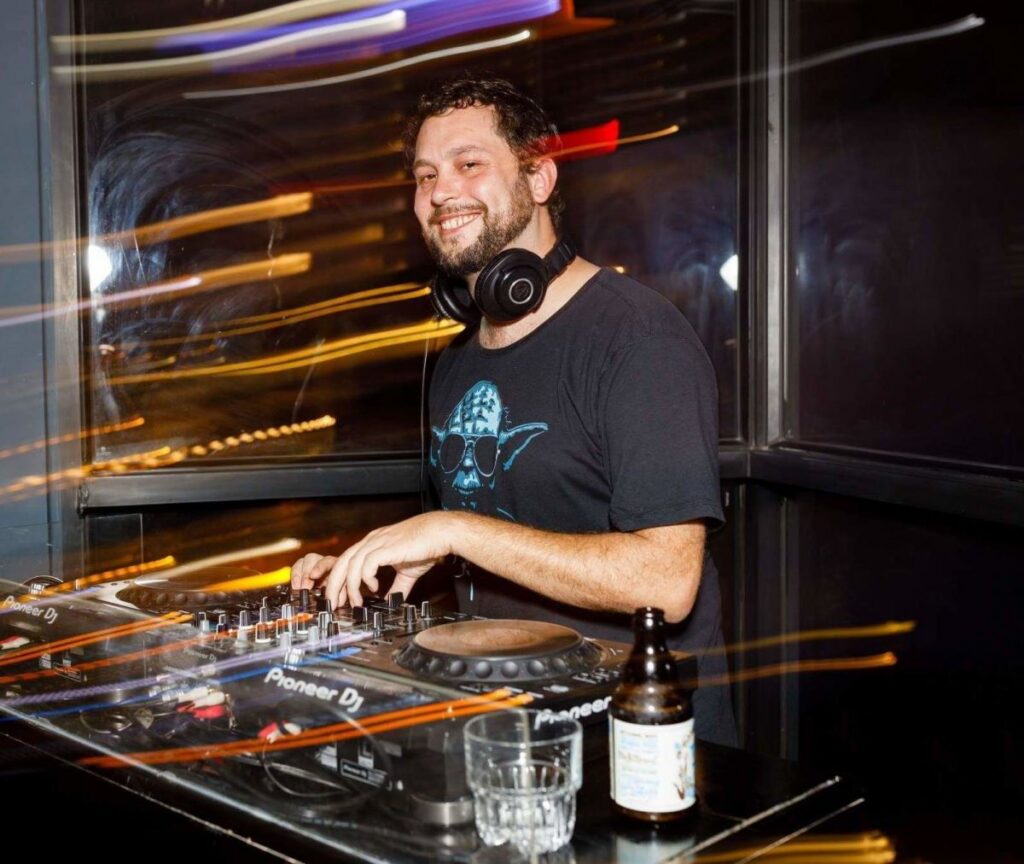 Yushka performs behind the decks with headphones around his neck during a Funk, Breaks and Hip Hop-focused DJ set.