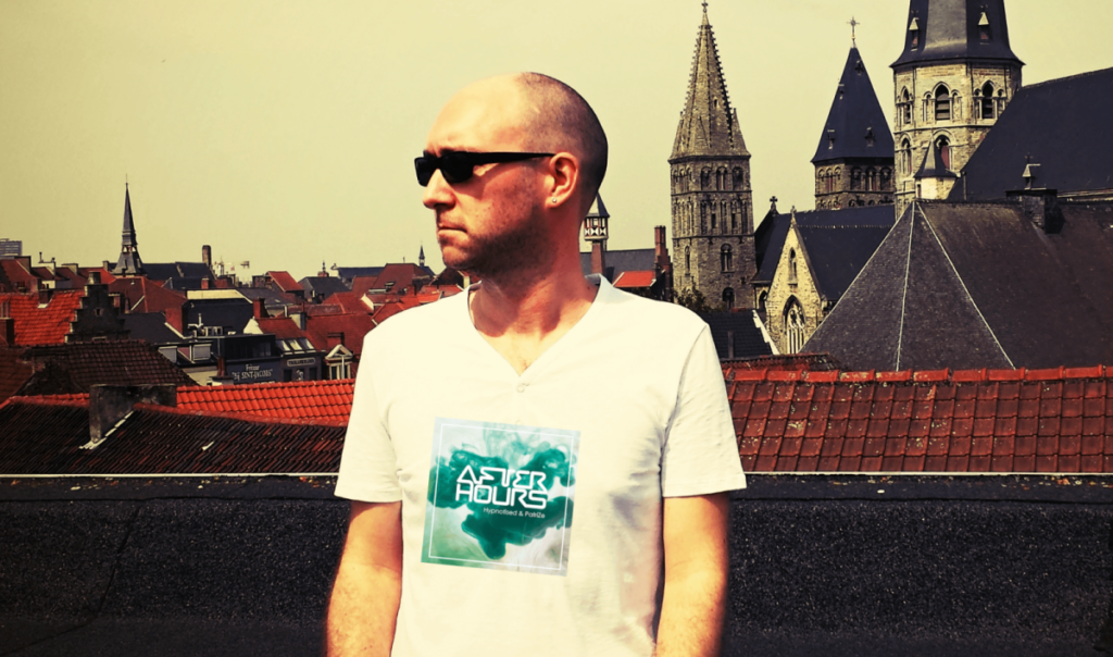 Hypnotised wearing sunglasses and an After Hours T-shirt on a rooftop with red-tiled buildings and church towers in the background.