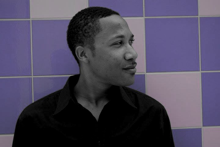 DJ Gerard wearing a black shirt and looking to the left in front of a purple and grey tiled wall.