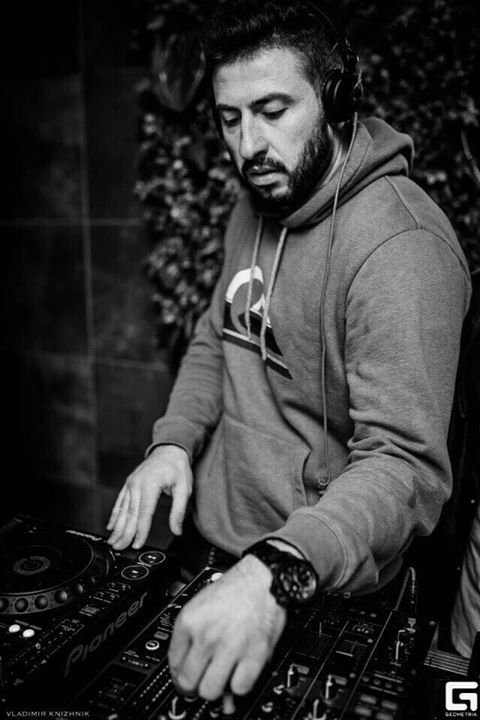 Black-and-white image of Andrey Manjinn wearing headphones and a hoodie while performing on Pioneer DJ equipment at an event.