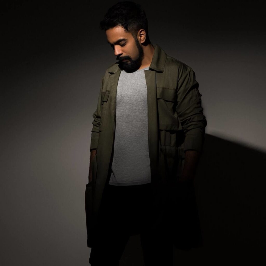 Future Culture, also known as Daniel Rajan, looking down while wearing a grey T-shirt and dark green jacket against a shadowed studio background.