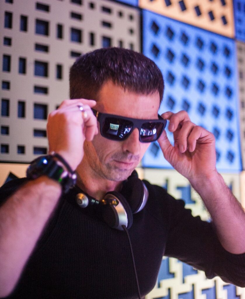 Goodika adjusting his sunglasses while wearing headphones around his neck during a performance.