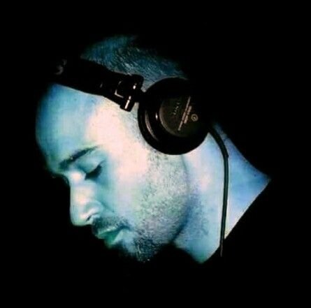 Green-tinted portrait of Sylk Poletti wearing headphones and looking down against a black background