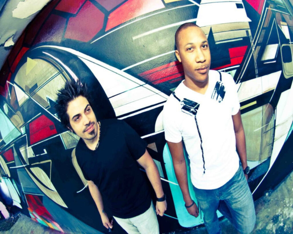Jose Norat and Gerard standing in front of a colourful geometric graffiti wall.