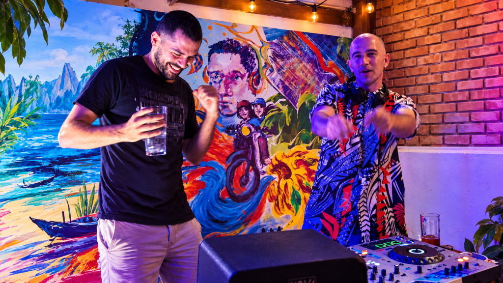 Badaboom founders Bipolar Bear and G Nomad performing together in Da Nang, Vietnam, with DJ equipment, colourful stage lighting and a vibrant mural behind them.