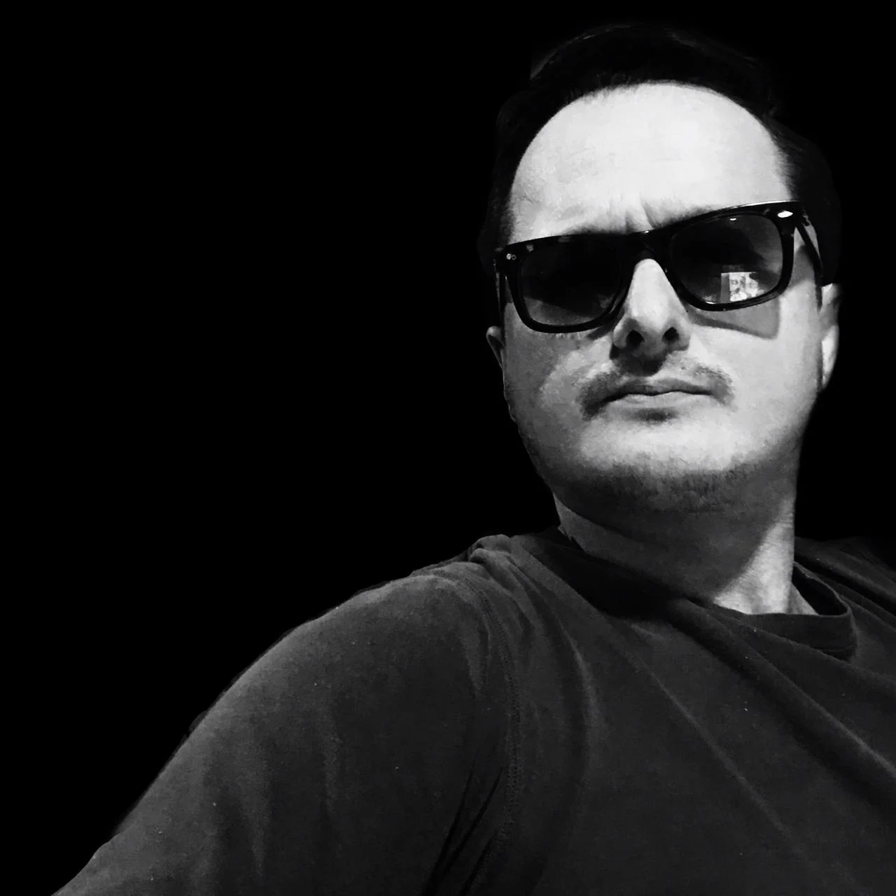 Colombian DJ and Producer Bustamante in upper body shot wearing sunglasses, black and white image.