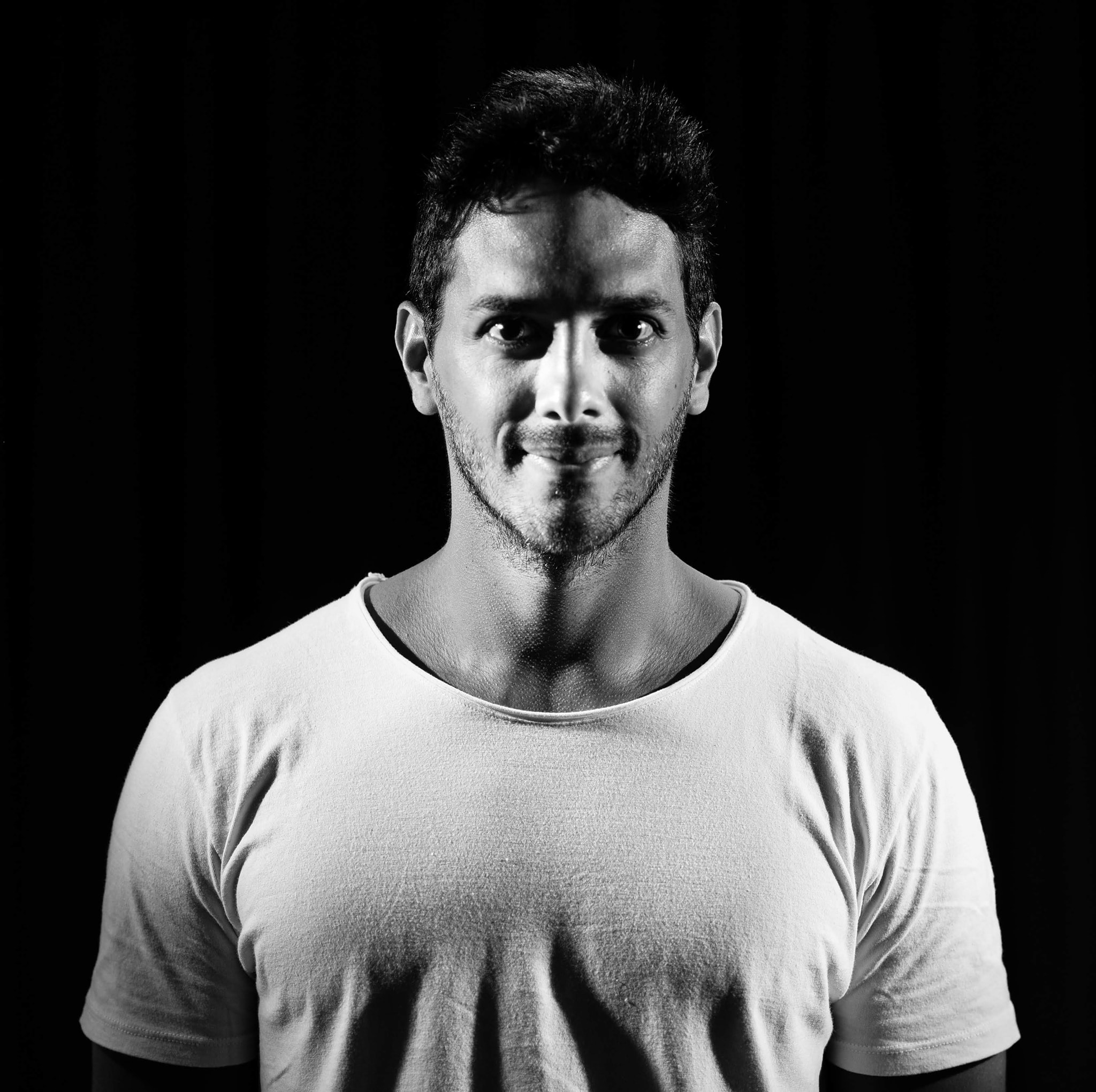 Argentinian DJ and producer Erich LH standing smiling at camera in studia shot with a black background, black and white image.