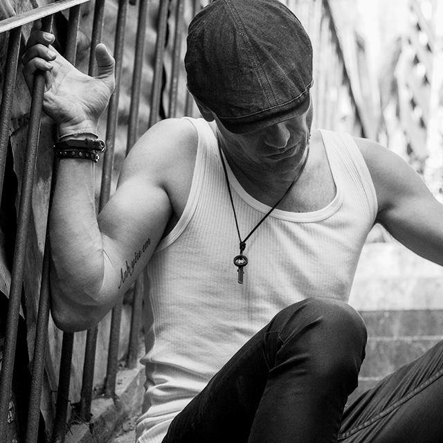 Danish DJ and producer Eskerod sitting on stairs looking down wearing a flat cap, black and white image.