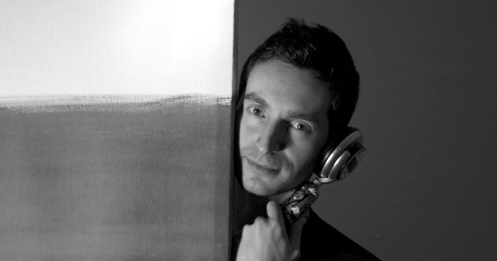 Italian DJ and Producer Inve standing behind a door looking from side with monophone against his ear, black and white image