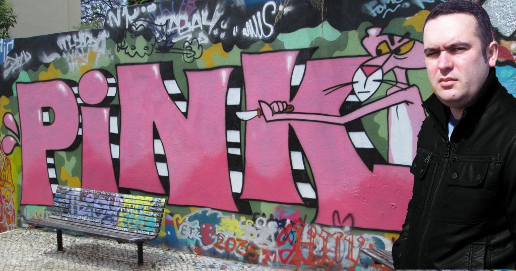 Portuguese DJ Joshua standing in front of Pink Panther graffiti in Lisbon, colour image.