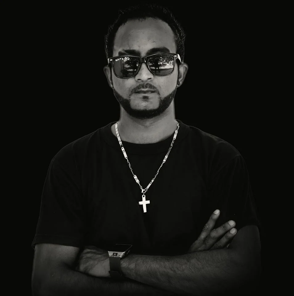 Sri Lnakan DJ Black Jay standing with arms crossed and wearing sunglasses, black and white image.
