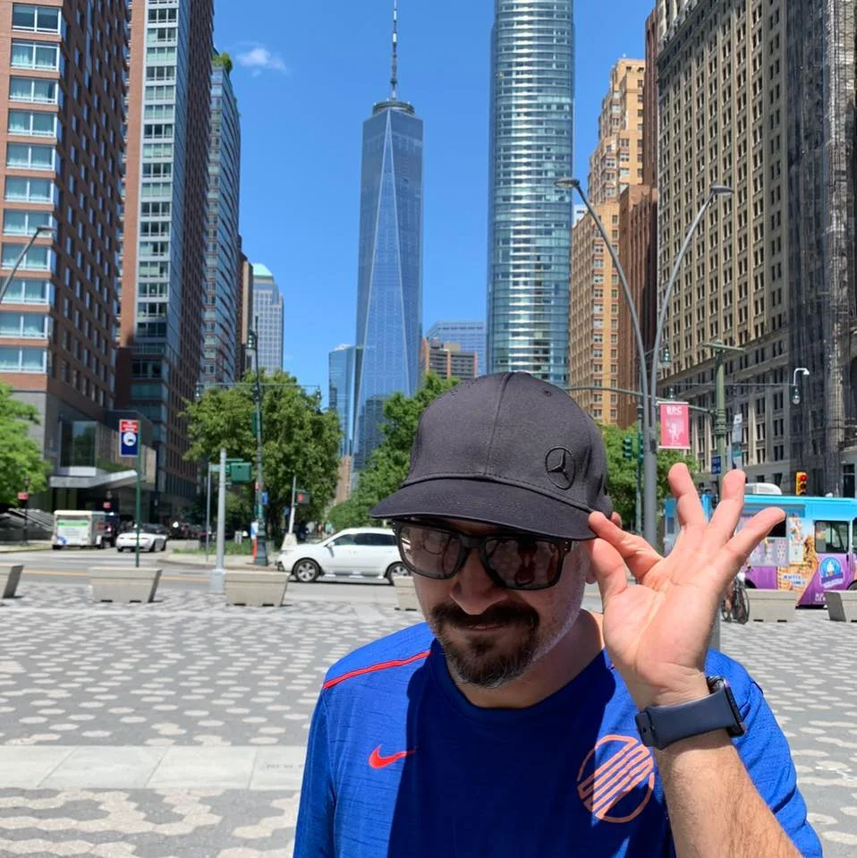 American DJ MPSoup lookimng at camera weeraing sunglasses and a cap with his logo with his left hand on the peak, colour image.