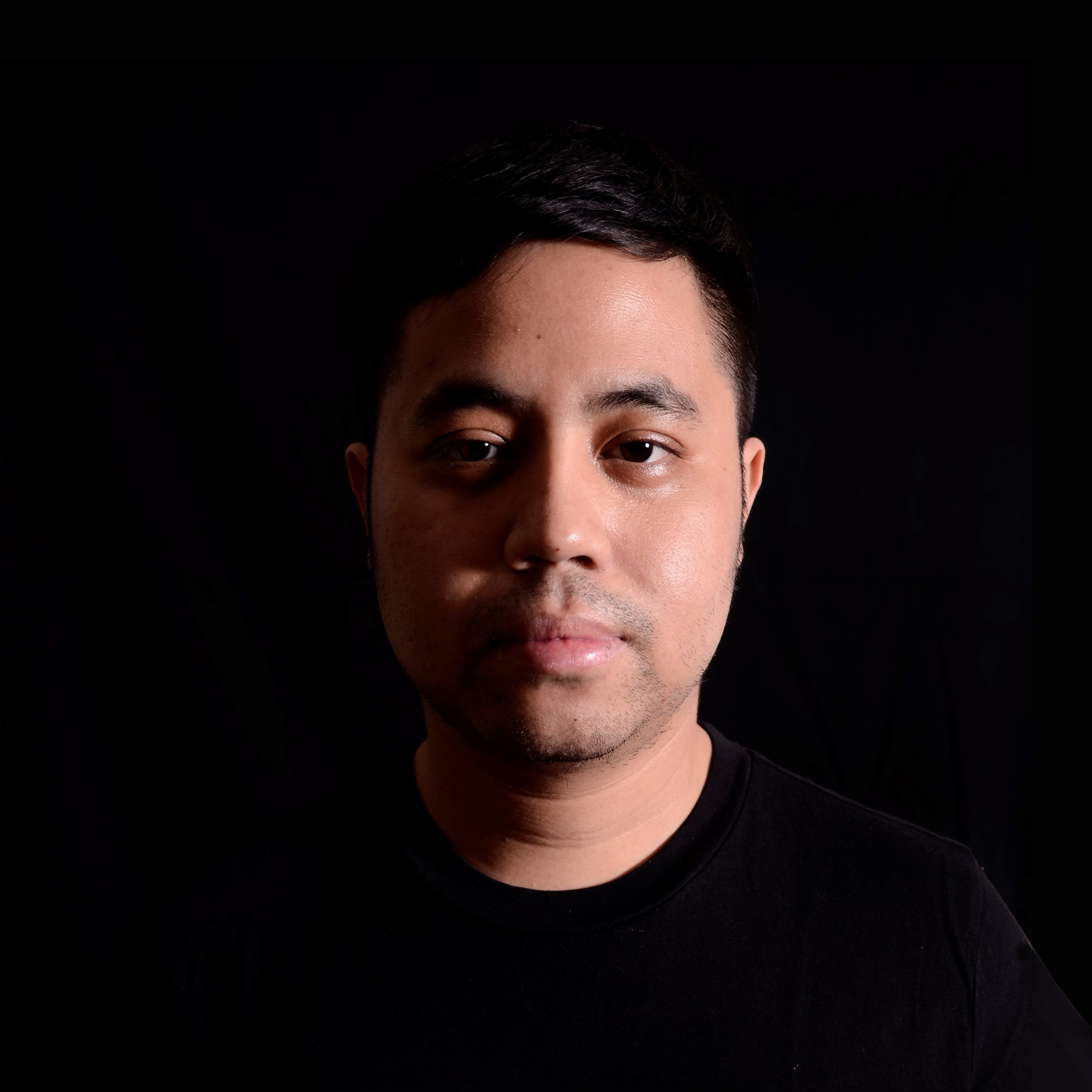 Indonesian DJ and Producer Nandi standing in darkened room looking at camera in upper body shot, colour image.