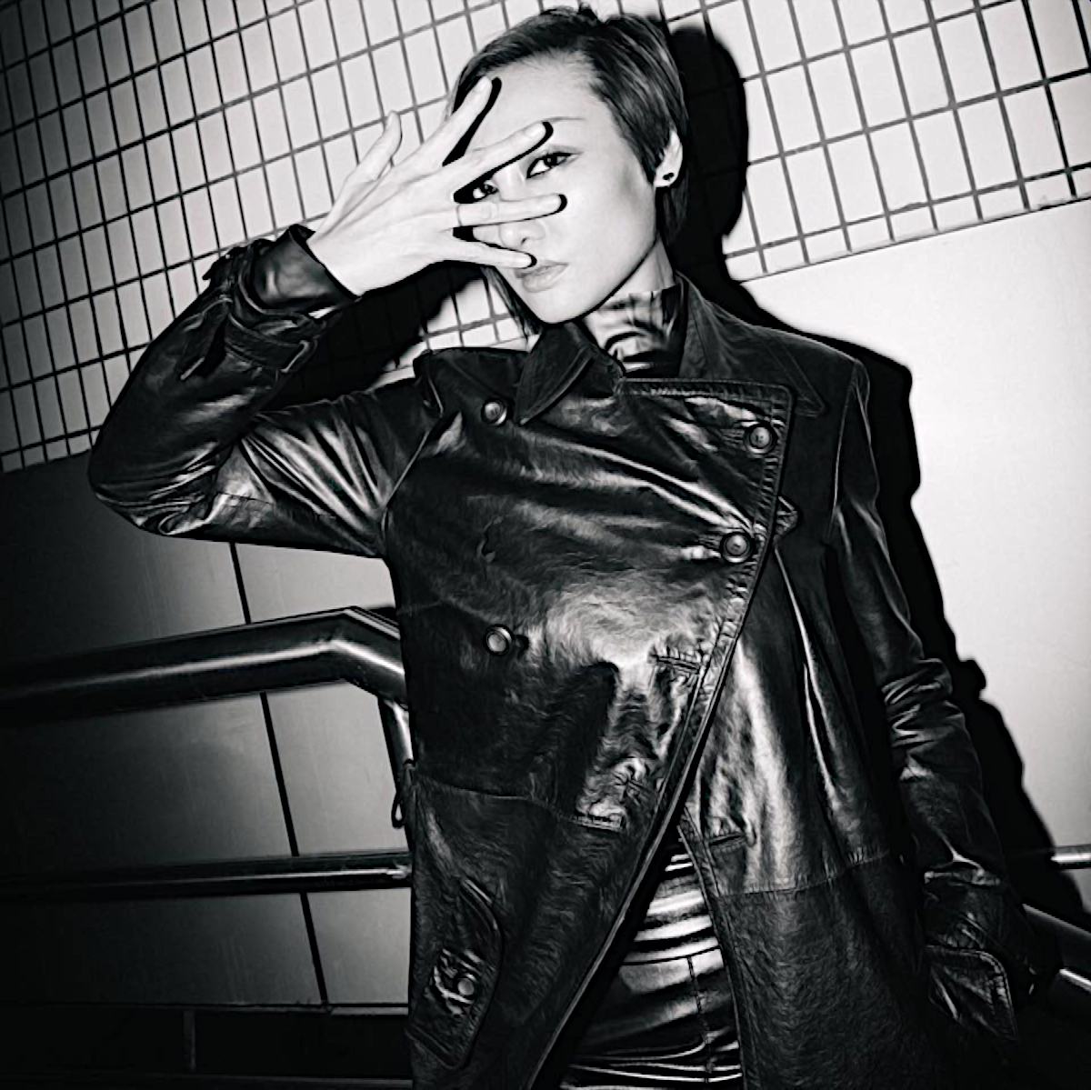 Chinese dJ and producer Jasmine Li standing in subway starwell with right fingers open in front of her face, black and white image.