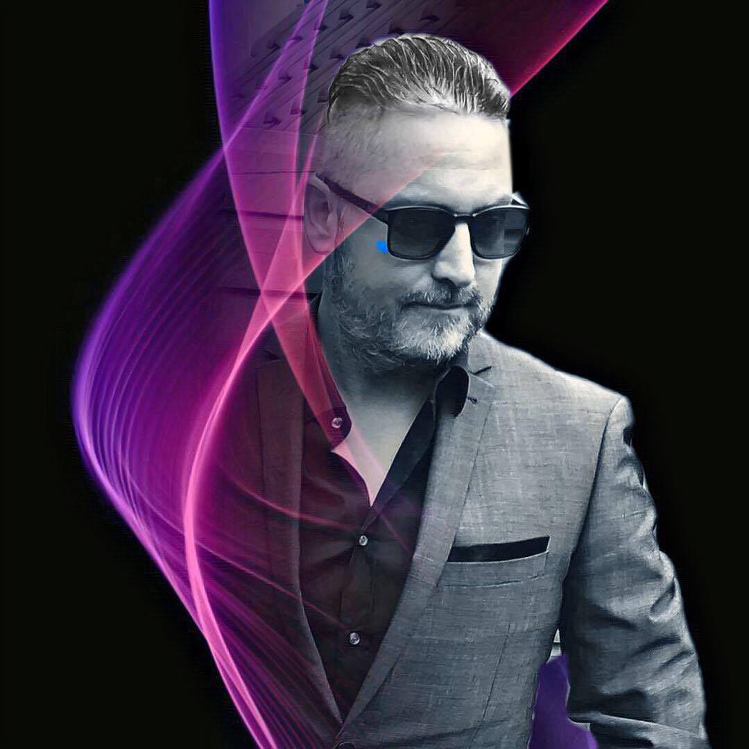 Dutch DJ, producer, and record label owner Roy Malloy standing wearing sunglasses and wearing a suit jacket, purple light going up in a swirl against a black and white image.