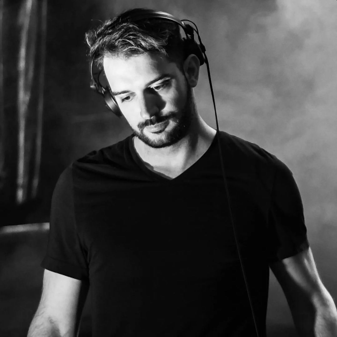 Argentinian DJ and producer Facundo Borras standing looking down and wearing headphones in upper body shot, black and white image.