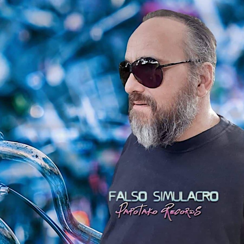 Argentinian DJ and producer Falso Simulacro standing wearing sunglasses whilst looking right with Papotako Records logo on his T shirt, colour image.