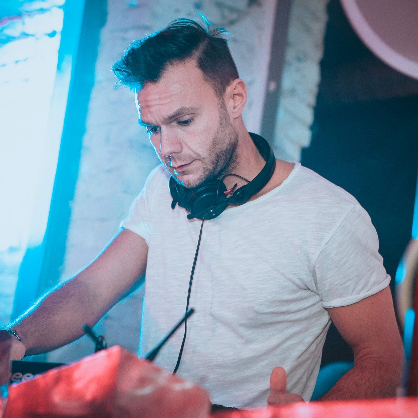 Italian DJ and Producer Andrea Mirgone standing with headphones around neck whilst performing at a venue, colour image.