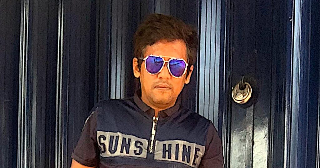 Indian DJ Psy Inertia standing in front of shutter wearing sunglasses, colour image.