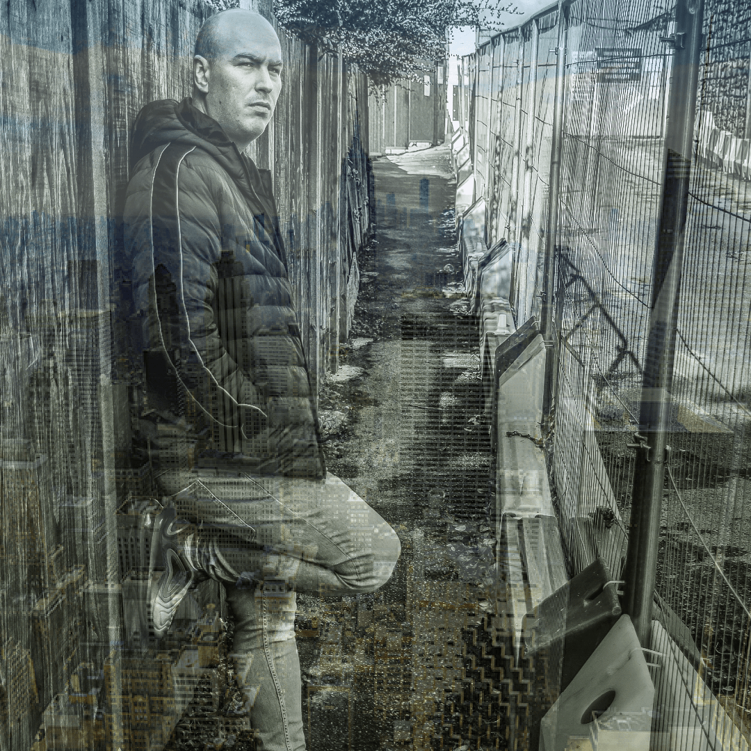 Irish DJ and producer Glenn Molloy leaning against wall with chainmail fence in front of him, black and white image