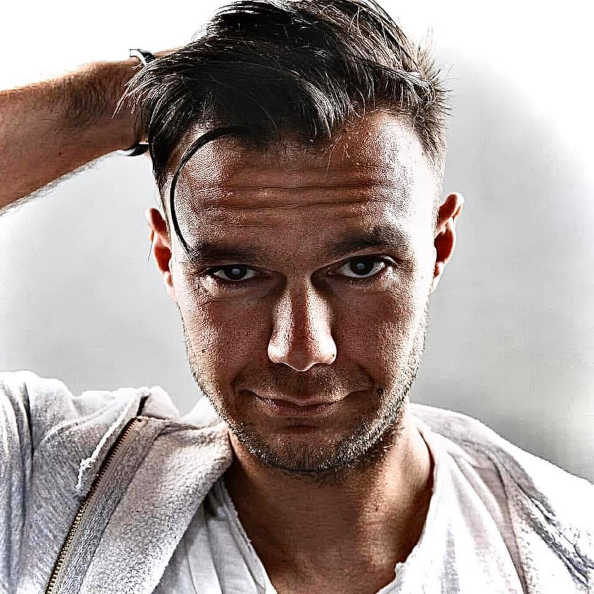 Italian DJ and Producer Andrea Mirgone part of TENET looking directly at camera with a smirk and his right hand behind his head, colour image.
