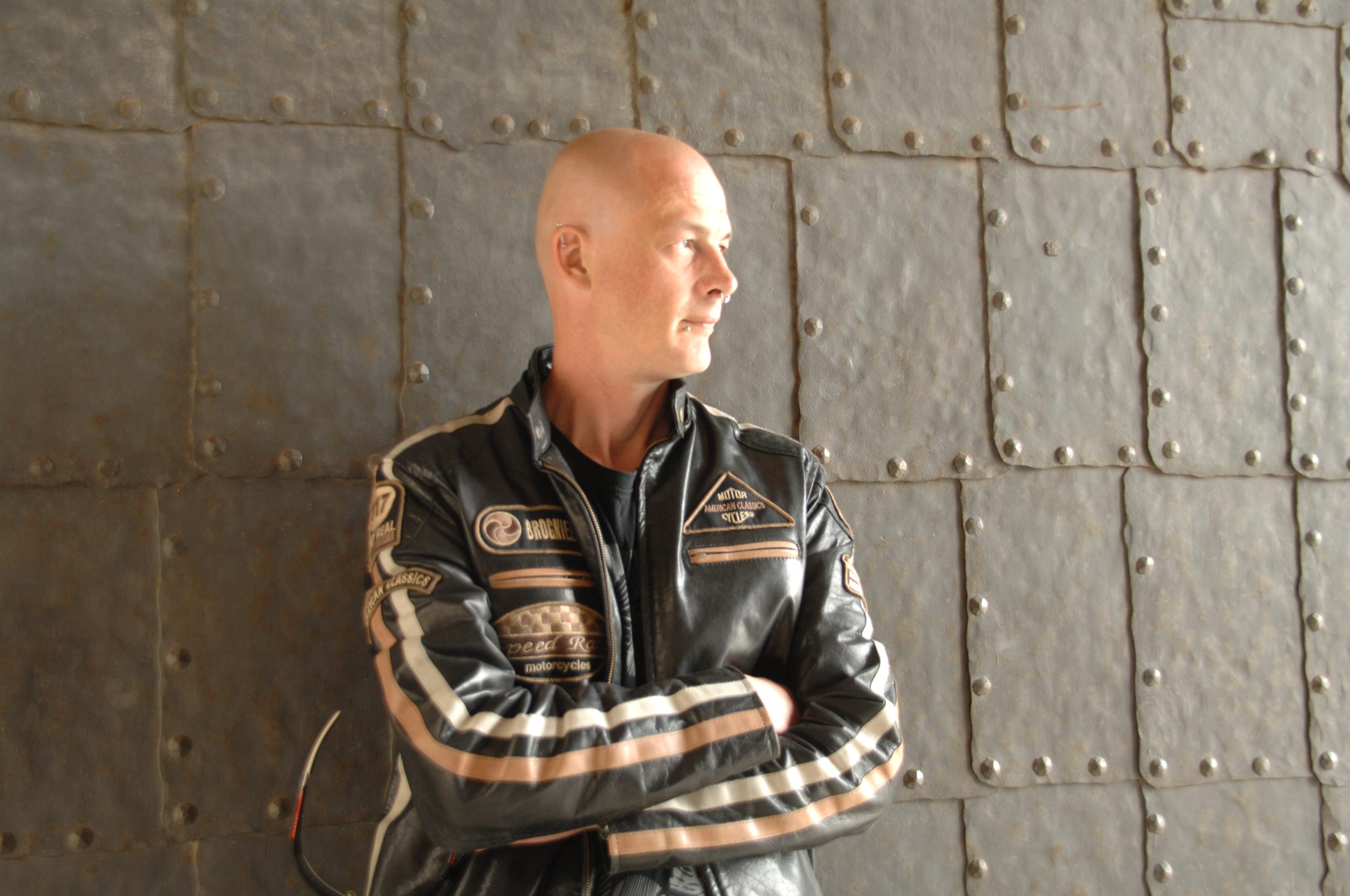 German Dj and producer Chris van Deer standing against wall wearing a coat, colour image.