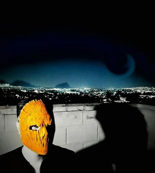 Mexican DJ and Producer Muuk wearing a facemask and standing on a rooftop at night in Mexico City, colour image.