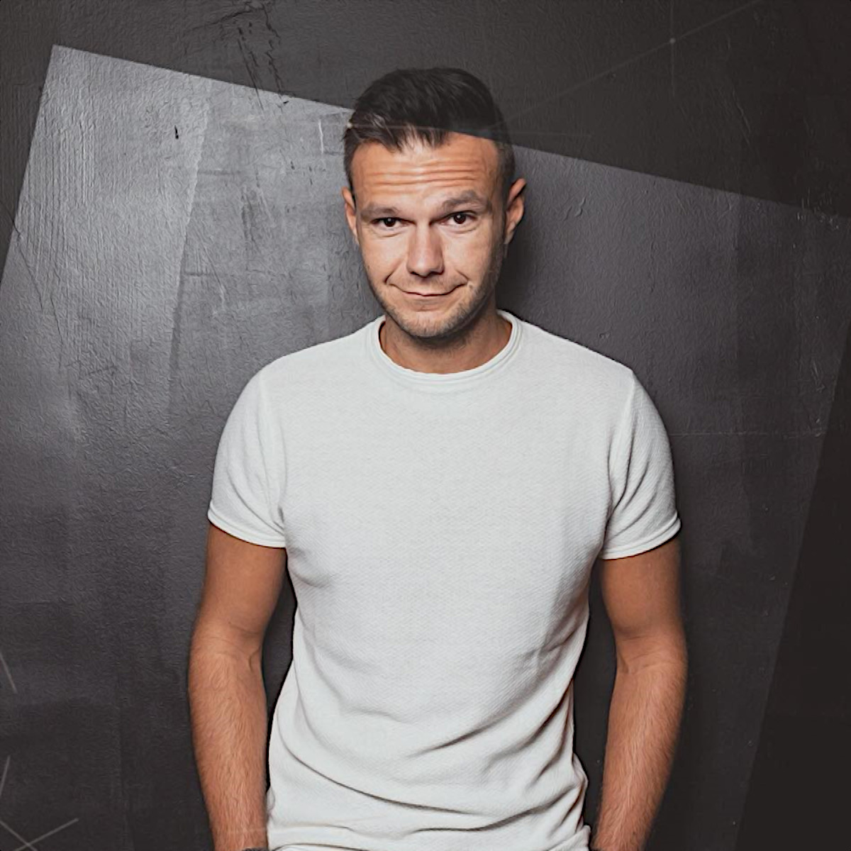 Italian DJ and Producer Andrea Mirgone standing with his hands in his pockets and smiling at camera in front of a black background, colour image.
