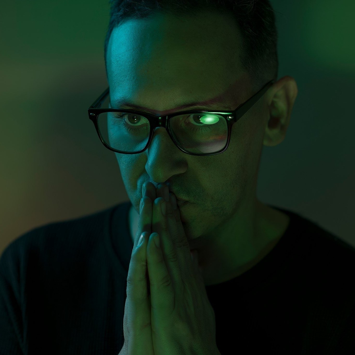 DJ and Producer Alex Efe with his hands together in prayer kissing his upper fingers with green lighting.