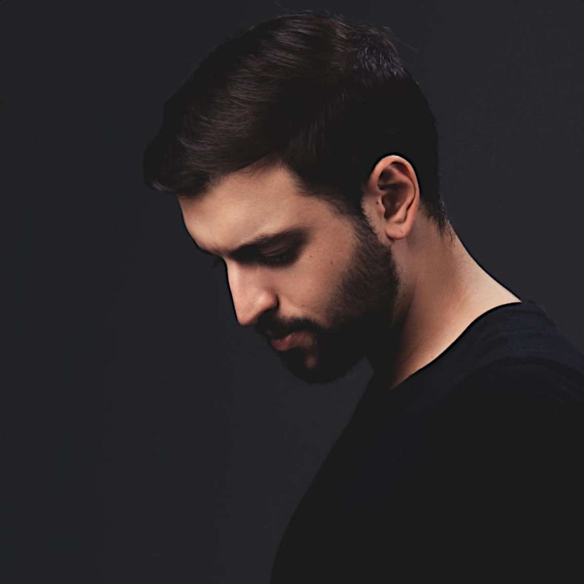 Brazilian DJ and producer Matt Oliver in side profile picture looking down and donning a beard, colour image.