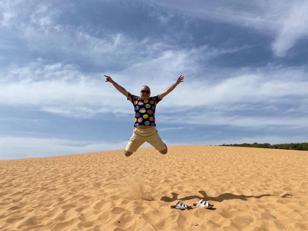 Italian DJ and producer Marco Mei jumping arms outstretched at Mui Ne Sand Dunes, Phan Thiet, Vietnam, colour image.