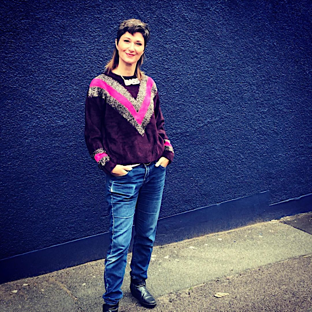 British DJ O.P Groover standing wearing a sweater and jeans in front of a wall in London, colour image.
