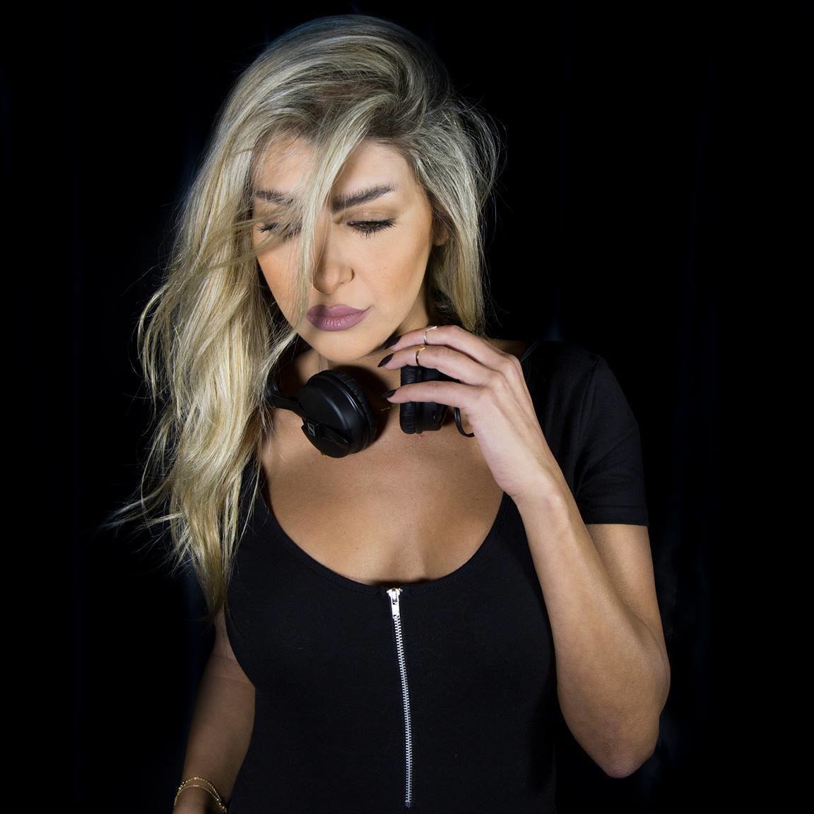 Female Lebanese DJ Paam wearing headphones around her neck black background.