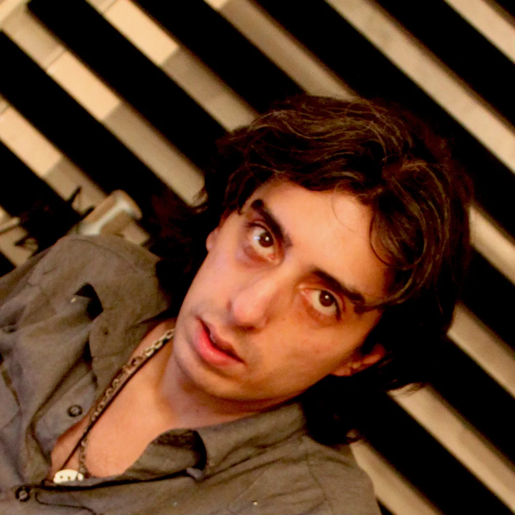 Portrait of Iranian DJ and producer Dadgar, co-founder, manager and A&R of McCarty Records, looking towards the camera against a striped background.