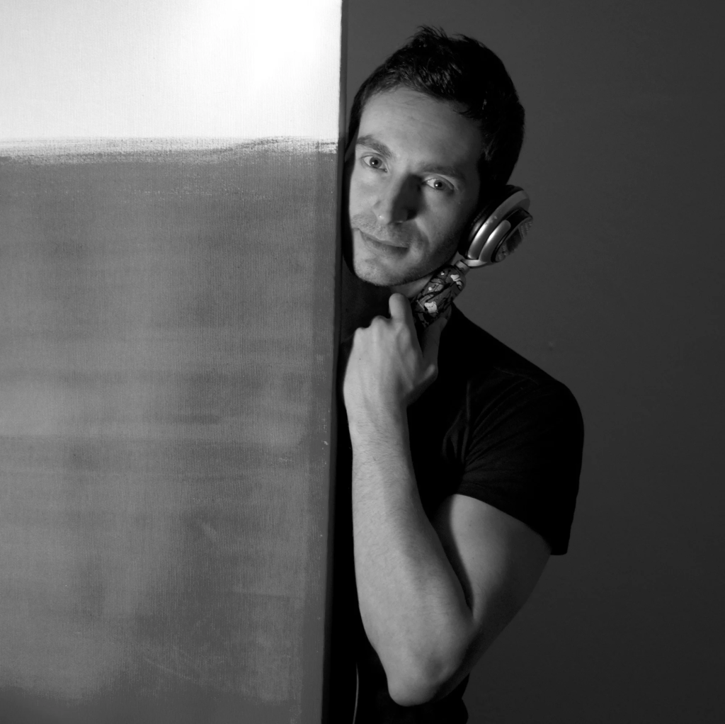 Italian DJ and Producer Inve standing behind a door looking from side with monophone against his ear, black and white image.
