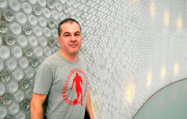 Italian DJ and producer Marco Mei standing in front of wall made with bottles, colour image.