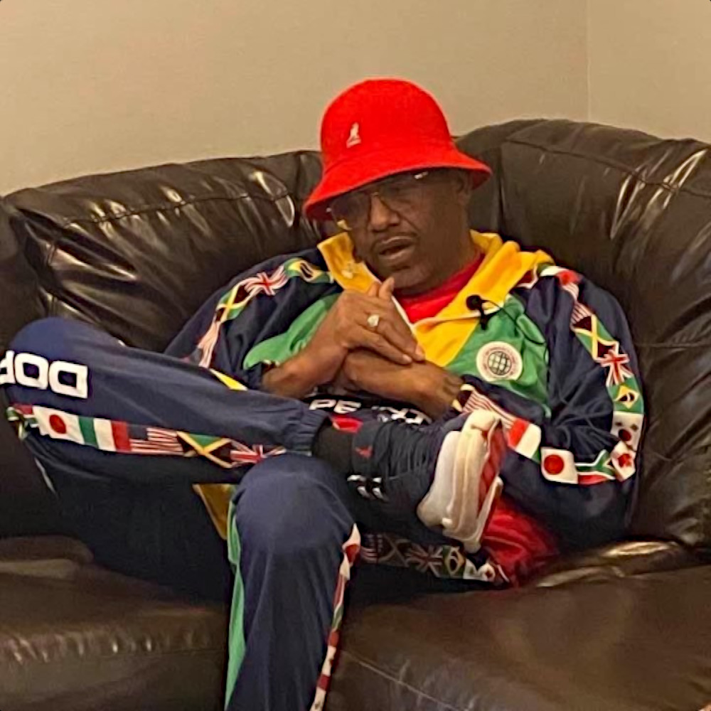 American rapper and producer RBX sitting in a chair wwearing hip hop wear, colour image.