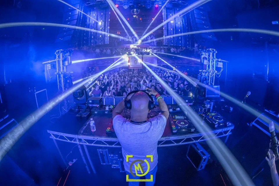 DJ Graham Gold performs at Peach in London, shown from behind the decks facing a packed crowd under blue club lighting and stage lasers.