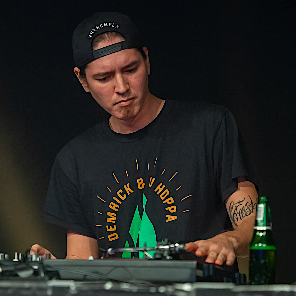American dJ andf producer DJ Hoppa performing on turntables at an event wearing a baseball cap backwards, colour image.
