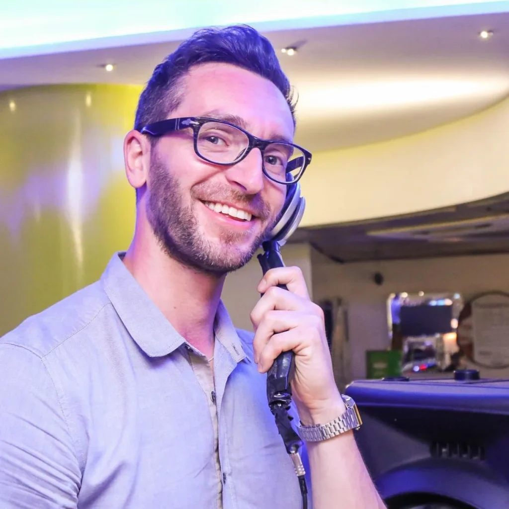 Italian DJ and producer Inve holding monophone to left ear and smiling at camera, colour image.