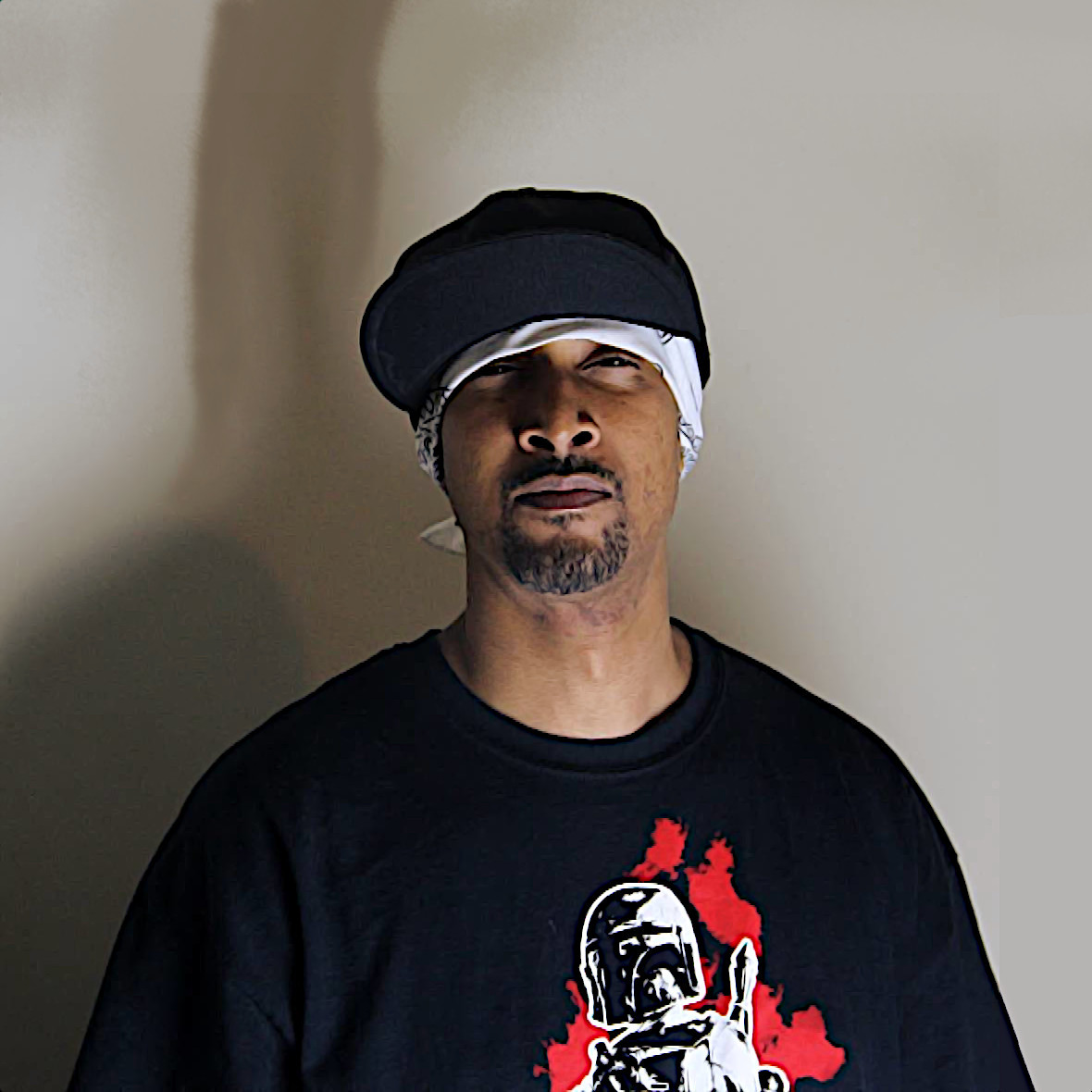 United States Rapper and producer Pacewon standing looking at camera wearing a white bandana and a baseball cap with a Boba Fett Sweater, colour image.