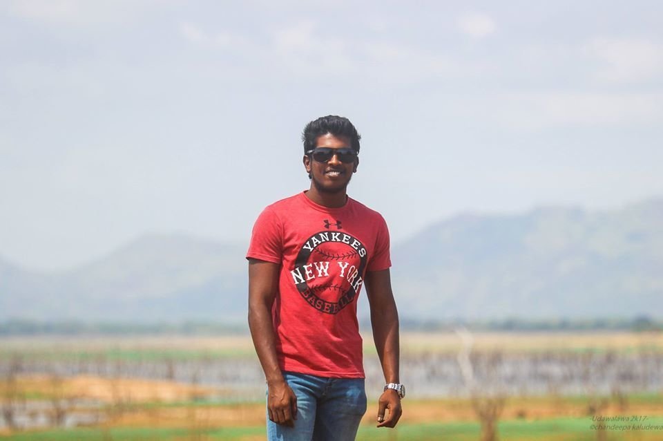 Sri Lankan DJ Kaludewa standing in the countryside in Ceylon wearing sunglasses in colour.