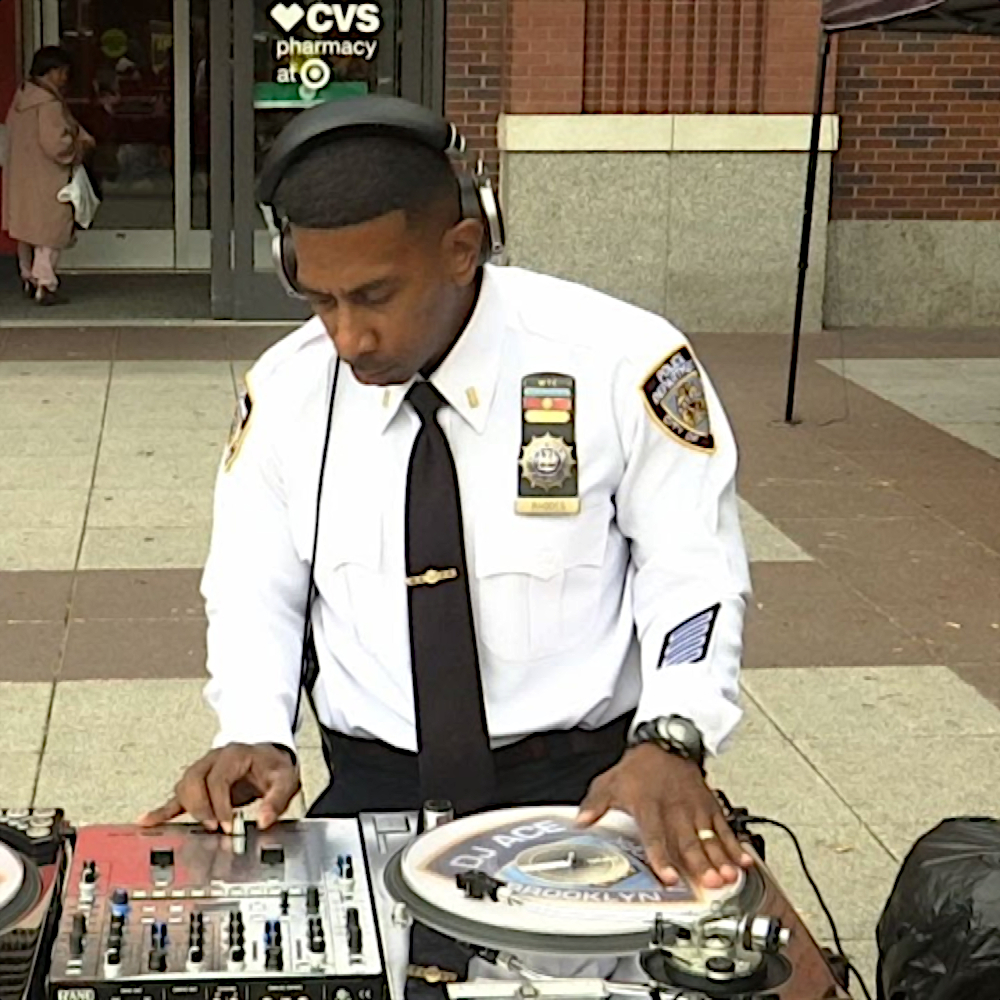 American DJ and producer DJ Ace The Cut Lieutenant performing in New York outside a pharmacy in his New York Police Department (NYPD) uniform, colour image.