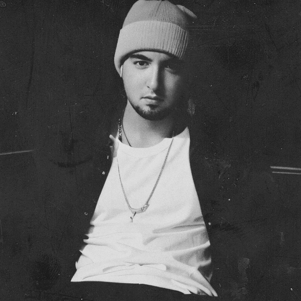 Italian DJ and producer Daniel Kaiser Malengo sat down wearing a beanie hat and a jacket in a vintage effect photo, black and white image.