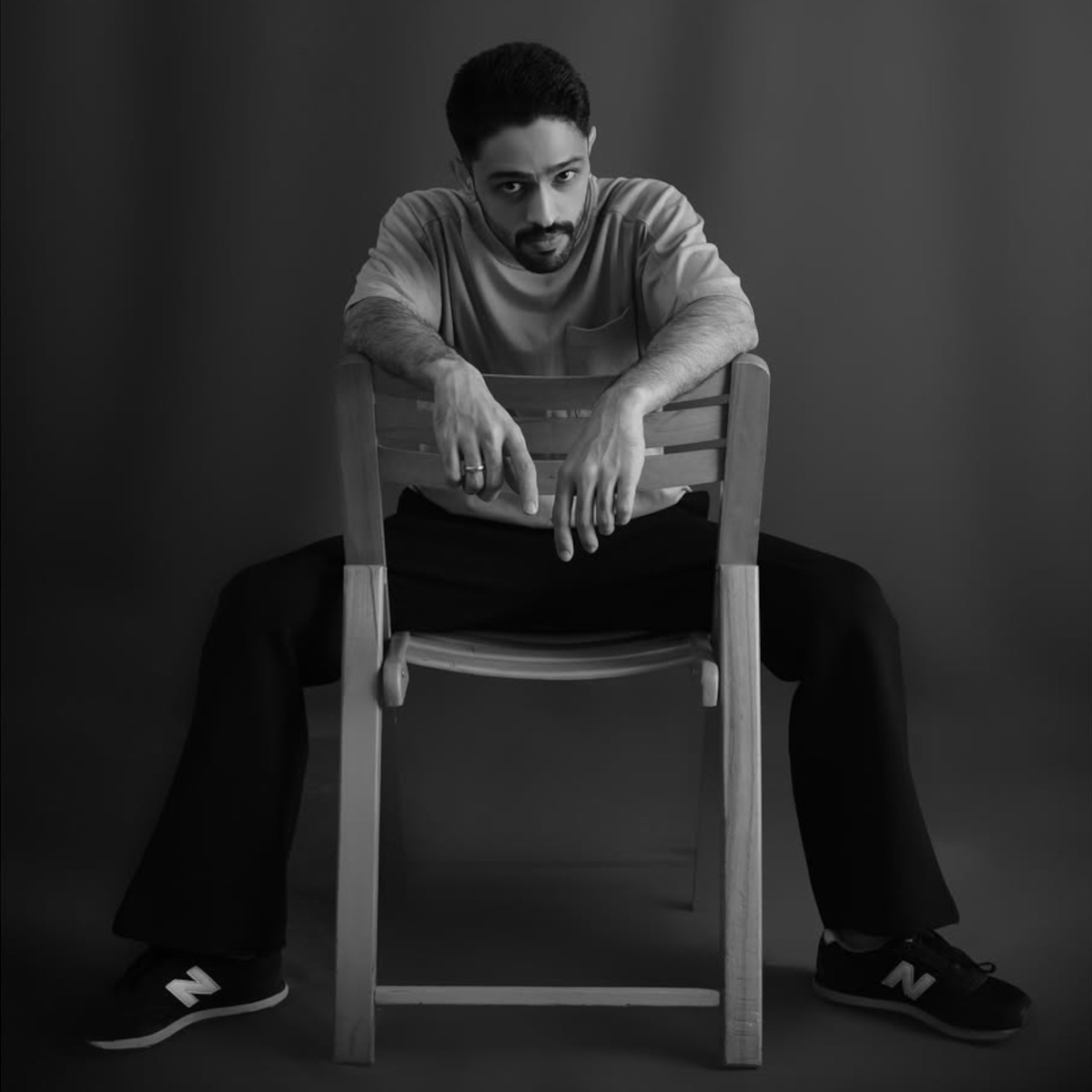 Pakistani DJ and producer Hamza Malik sitting on a chair backwards with his arms on the top of the backrest, looking seriously at the camera, black and white image.