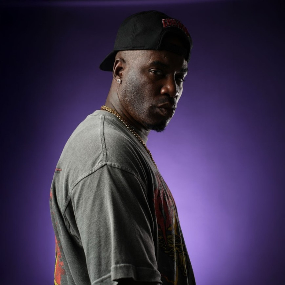American rapper Casablanca The Gawd looking over his right shoulder at the camera wearing a baseball cap backwards, colour image.