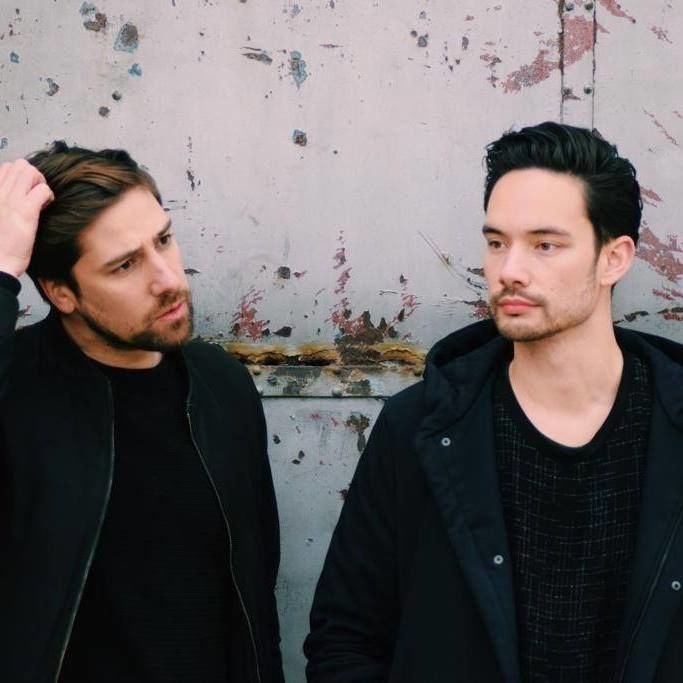 Belgian DJ and production duo Arkaene standing next to each other in front of a wall, colour image.