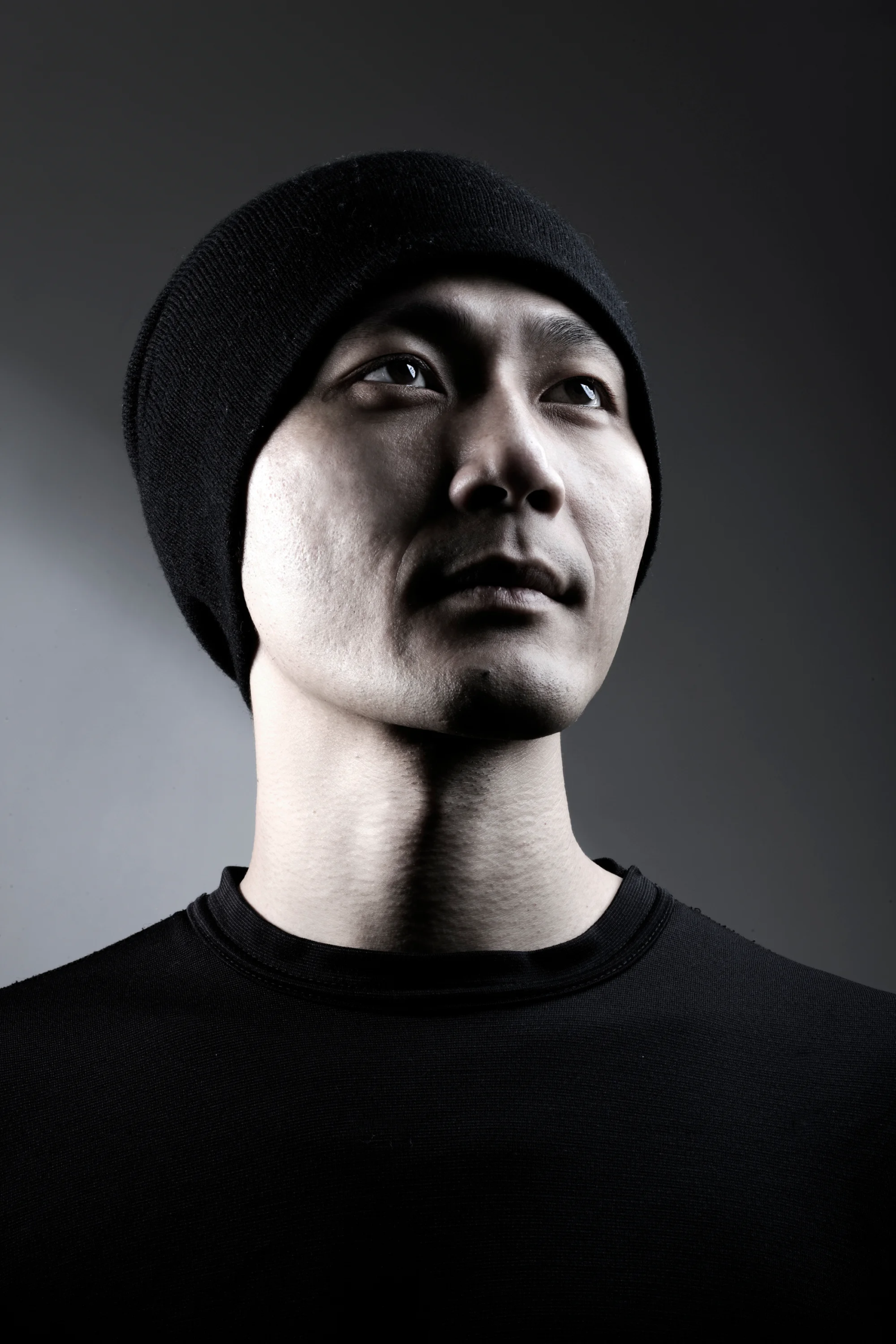Taiwanese DJ and producer Vertigo standing wearing a beanie hat and looking up, upper body shot in colour.