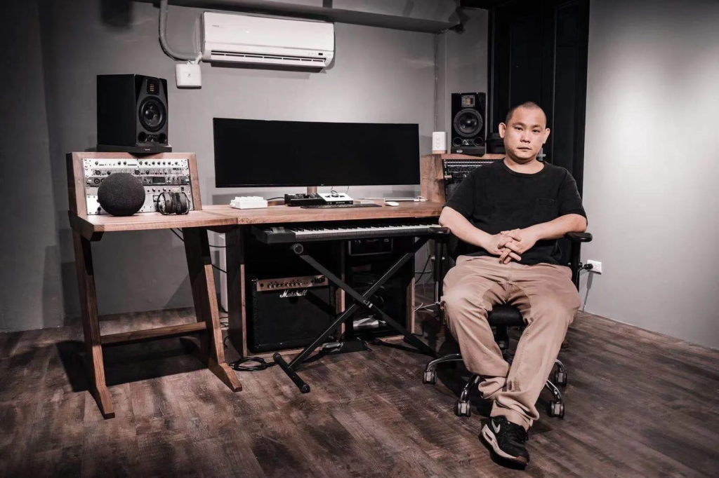 Taiwanese DJ Neil sitting in a chair in a music production studio, colour image.