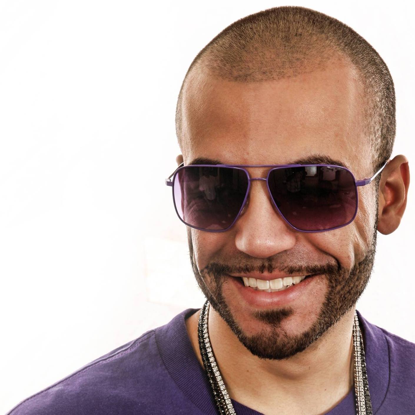 American DJ and producer DJ Pain 1 a.k.a Pacal Bayley smiling in a headshot wearing sunglasses and a chain and donning a neatly cropped short beard and hair in colour image.